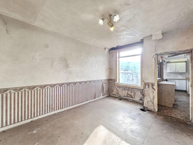 The rear dining room looking through to a dated kitchen, with plaster missing beside the window and the floor down to the screed