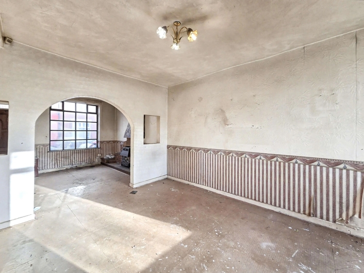 The through lounge, stripped back to bare concrete floor, with striped dado paper and an archway through to the front room