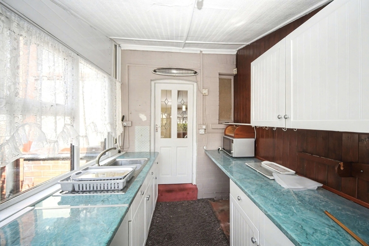 A narrow galley kitchen with green marbled worktops, lace curtains and crockery still left on the drainer