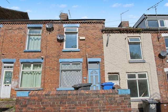 A red brick terraced house with a blue front door, wheelie bins by the wall