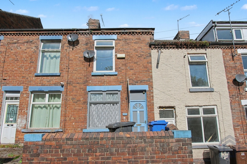 A red brick terraced house with a blue front door, wheelie bins by the wall